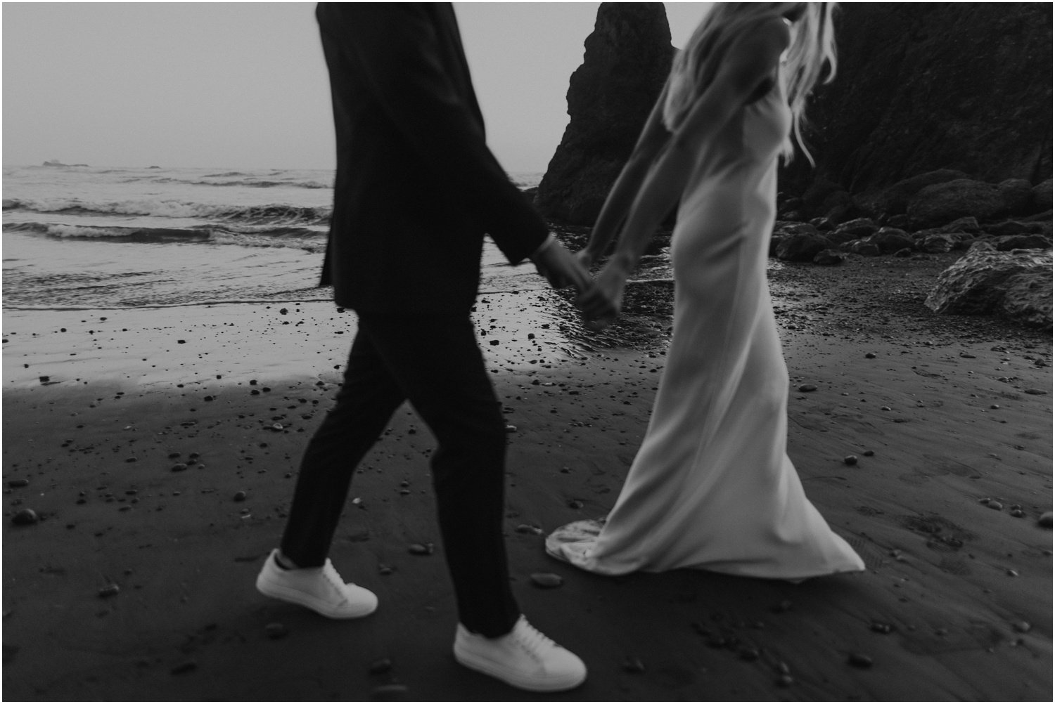 black and white photo of married couple walking along the washington coast at sunset