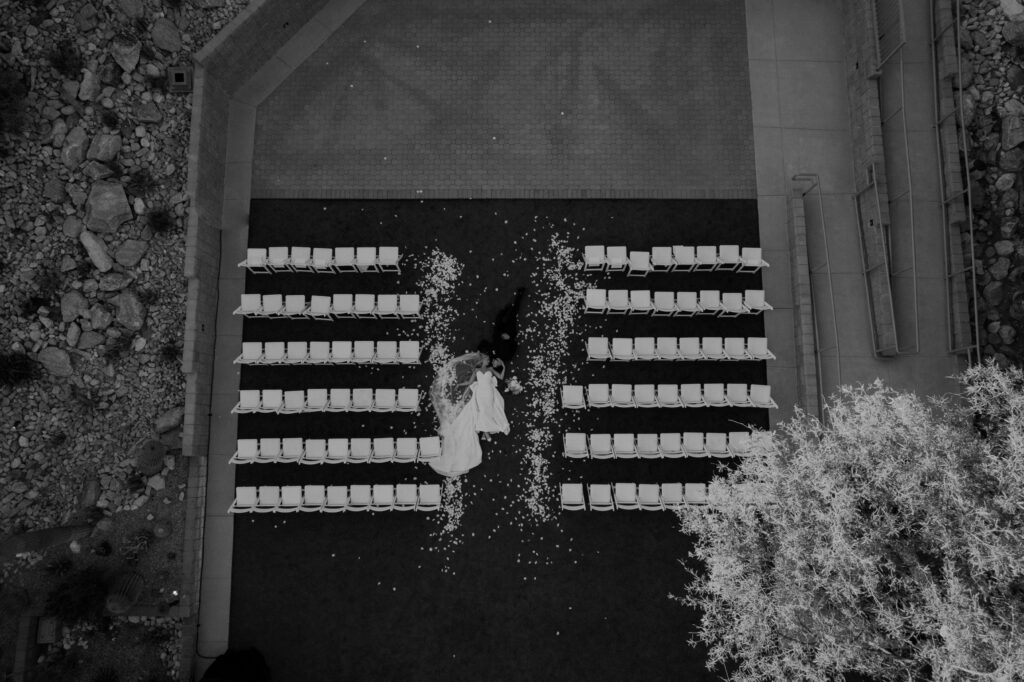 arial shot of a bride and groom laying on the ground in the middle of their ceremony aisle. drone shot of bride and groom. black and white photo of an arizona wedding