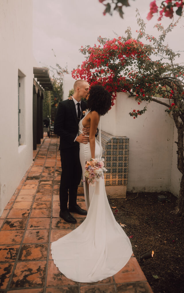 bride and groom kissing underneath red flowers